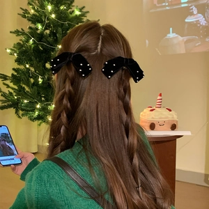 Pair of black velvet bow hair clips with pearls shown on braided hair in warm setting