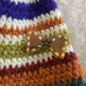 Detailed close-up of a knitted bow hair clip with a resin star button and colorful yarn