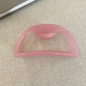 Detail showing pink cutout acetate hair claw clip with semi-circle design on beige fabric