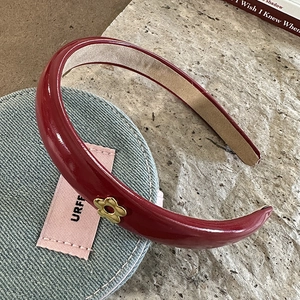 Macro detail of wine red PU leather headband featuring a golden floral metal accent charm