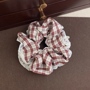 Detail view of a vintage red checkered scrunchie with delicate white lace edges on wood