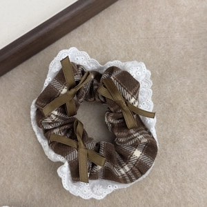 Detail view of brown plaid scrunchie with white lace edges and olive green bows