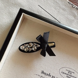 Close-up of black satin bow hair clip with sparkling rhinestones and gold LOVE plate