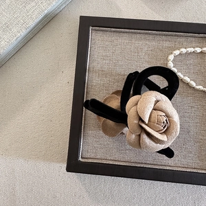 Gros plan d'une pince à cheveux camélia beige avec bordure en velours noir