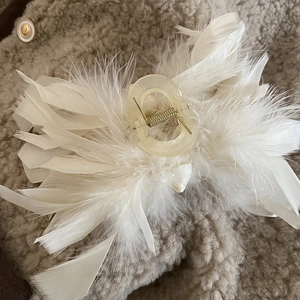 Close-up of elegant cream ostrich feather hair claw clip on beige wool fabric texture