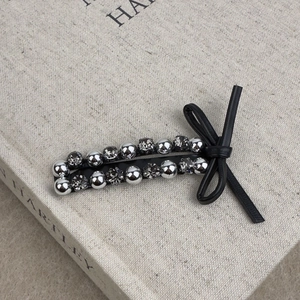 Detailed close-up of a leather bow hair clip with silver beads and grey rhinestones