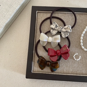 Handmade acetate bow hair ties in four colors displayed in an elegant wooden tray
