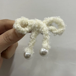 Detail of cream white knit bow hair clip featuring elegant faux pearl charms and wool texture