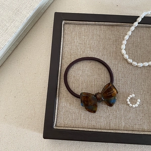 Detail of dark brown elastic hair tie with amber tortoiseshell bow and gold text logo