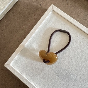 Dettaglio ravvicinato di un cuore in resina traslucida su elastico per capelli flessibile
