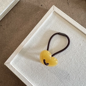 Dettaglio del ciondolo a cuore in resina gialla traslucida su un elastico marrone