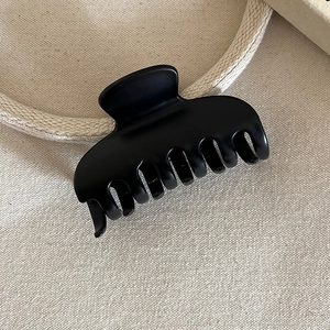 Detailed macro view of large matte black shark hair claw clip on beige fabric