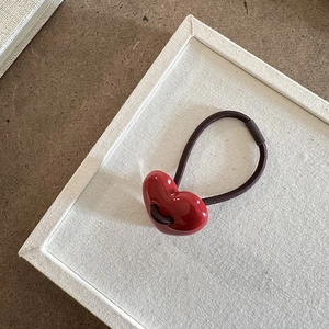 Dettaglio di un ciondolo a cuore rosso lucido su un elastico per capelli nero resistente