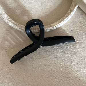 Detail of matte black shark hair claw clip with cross-twist design on beige canvas