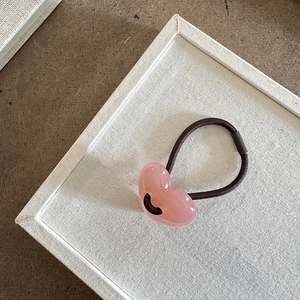 Dettaglio macro dell'elastico per capelli con cuore in resina rosa su tessuto bianco