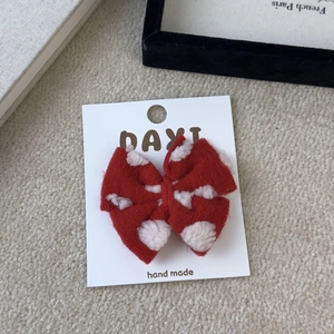 Detail of red knitted bow hair clip with white flower pattern on a white display card