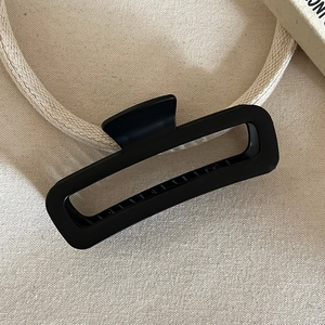 Close-up of matte black rectangular hair claw clip on beige canvas background