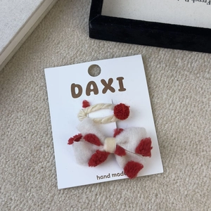 Detail view of handmade beige plush hair clip set with red pom-poms on display card