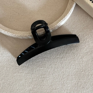 Detailed view of large matte black shark hair claw clip on neutral beige fabric