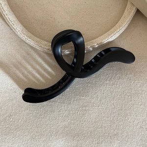 Close-up of matte black large shark hair claw clip with crossed curved design and texture