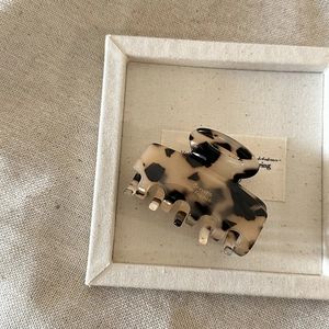 Elegant tortoiseshell acetate hair claw clip with gold label on beige fabric tray