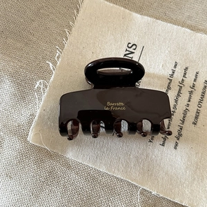 Close-up of tortoise shell pattern hair claw clip with golden France label on linen texture