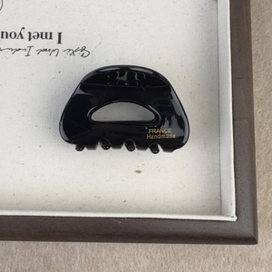 Glossy black acetate hair claw with hollow semicircular design and gold lettering