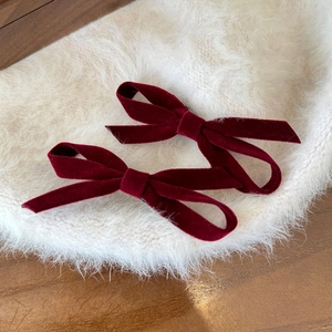 Macro shot of two wine red velvet bow hair clips on soft white faux fur background