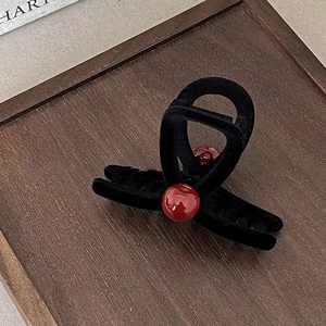 Black velvet hair claw clip with red pearls on a wooden tray, elegant winter accessory