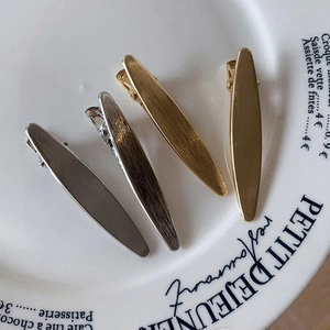 Set of 4 matte brushed metal leaf hair clips in gold and silver finish on a plate
