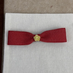 Détail d'une pince à cheveux nœud rouge avec une rose dorée en relief au centre