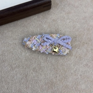 Détail d'une pince à cheveux en tweed rose avec nœud violet et pendentif cœur doré