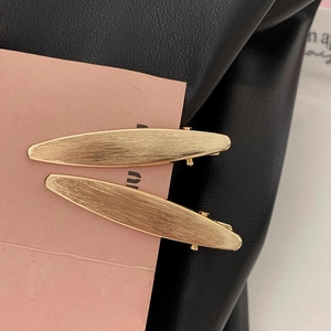 Macro detail of golden matte metal leaf hair clips with brushed texture on display card