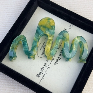 Detail showing wavy acetate hair claw with green and yellow marble patterns in box