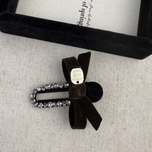 Detail of velvet bow hair clip with silver embossed logo and dark grey rhinestones