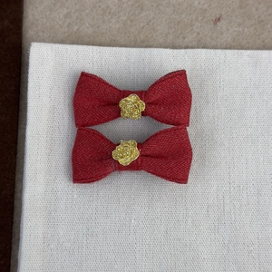 Détail de barrettes nœuds en tissu rouge ornées d'une décoration centrale de rose dorée