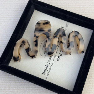 Macro detail of tortoiseshell acetate wave hair claw clip inside a minimalist jewelry box