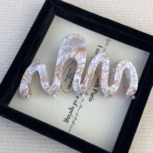 Detail shot of wavy acetate claw clip with cream marble pattern in a jewelry box