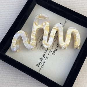 Macro detail of large acetate wave hair claw clip with creamy marble texture in a gift box