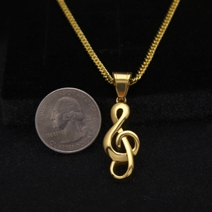 Pendentif clé de sol doré avec chaîne présenté à côté d'une pièce pour la taille
