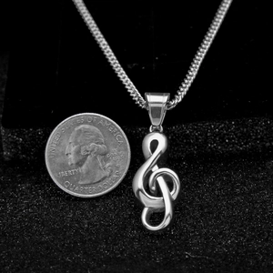 Pendentif clé de sol en argent avec chaîne à côté d'une pièce pour la taille