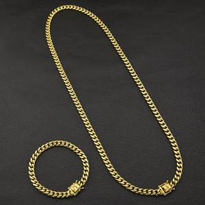 Detail shot of golden Cuban link necklace and bracelet set with square clasp on black background