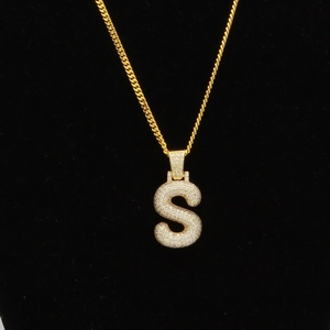 Gros plan sur collier chaîne cubaine dorée avec grand pendentif lettre S pavé de strass