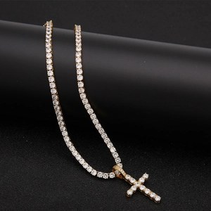 Close-up of gold-plated hip hop tennis chain with iced-out cross pendant on black surface