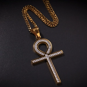 Gros plan du pendentif croix Ankh doré avec pierres étincelantes sur fond noir mat