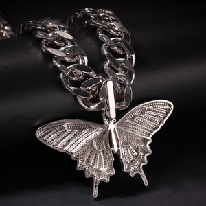 Detailopname van een zilveren vlinderhanger aan een dikke Cubaanse schakelketting met details