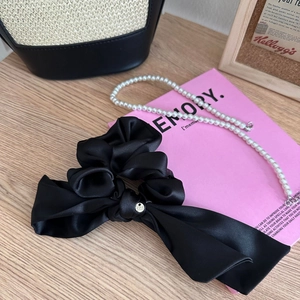 Dettaglio dell'elastico in raso nero con ciondolo in metallo e collana di perle elegante