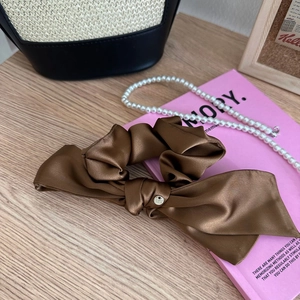 Dettaglio dell'elastico per capelli in raso marrone con ciondolo su libro rosa