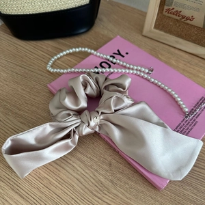 Dettaglio di scrunchie in raso champagne con fiocco e collana di perle chic