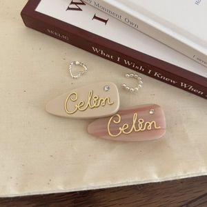 French style acetate hair clips with gold lettering and delicate earrings on linen background